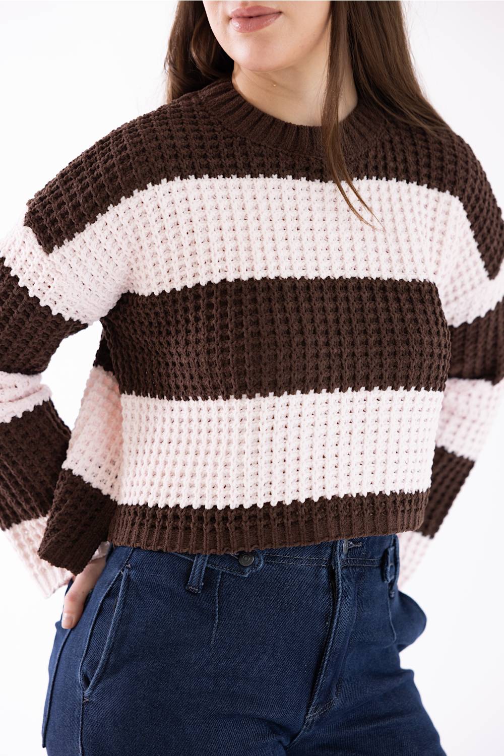A woman wearing a brown and cream striped knit sweater with dark blue jeans, shown from the chest down against a plain white background.