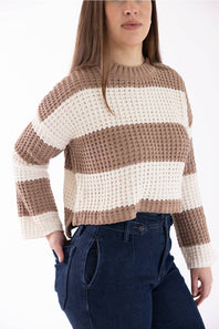 Woman wearing a Pink Rose wide tan-and-white-striped crewneck sweater with long sleeves, shown from a three-quarter side angle with her hand in her dark blue jeans pocket.
