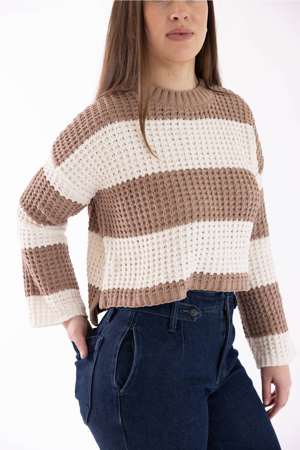 Woman wearing a Pink Rose wide tan-and-white-striped crewneck sweater with long sleeves, shown from a three-quarter side angle with her hand in her dark blue jeans pocket.