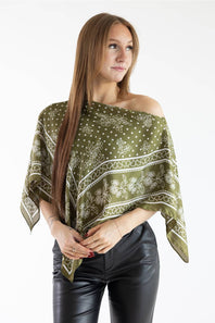 Medium shot of a woman modeling an off-the-shoulder olive green floral scarf poncho top with black leather pants.