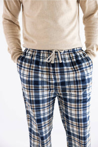 A person wearing blue, white, and beige plaid pajama pants with a white drawstring, paired with a beige knit sweater, shown from the chest down against a white background.