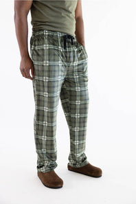 A person wearing green and gray plaid lounge pants with a black drawstring, paired with a green shirt and brown slippers, photographed against a plain white studio background.