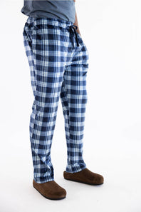 A person wearing blue and white plaid pajama pants with a drawstring waist, paired with a gray top and brown slippers, shown from the waist down on a white studio background.