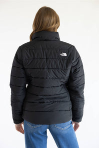A woman viewed from the back wearing a black puffer jacket with a white embroidered The North Face logo on the upper back, paired with blue jeans against a plain white background.