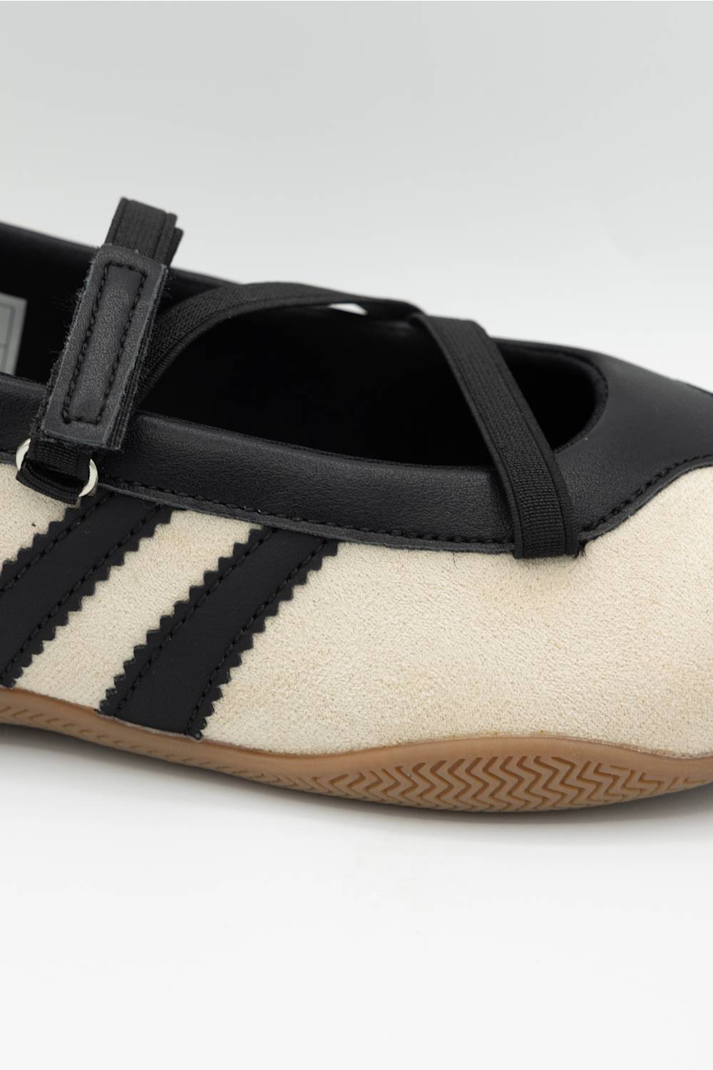 A close-up of a Mary Jane shoe featuring a cream suede upper, black leather trim and straps, three black stripes, and a brown gum sole.