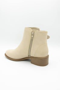 A beige faux-suede ankle boot with a side zipper, low block heel, and brown striped sole, shown from a rear three-quarter angle on a white background.