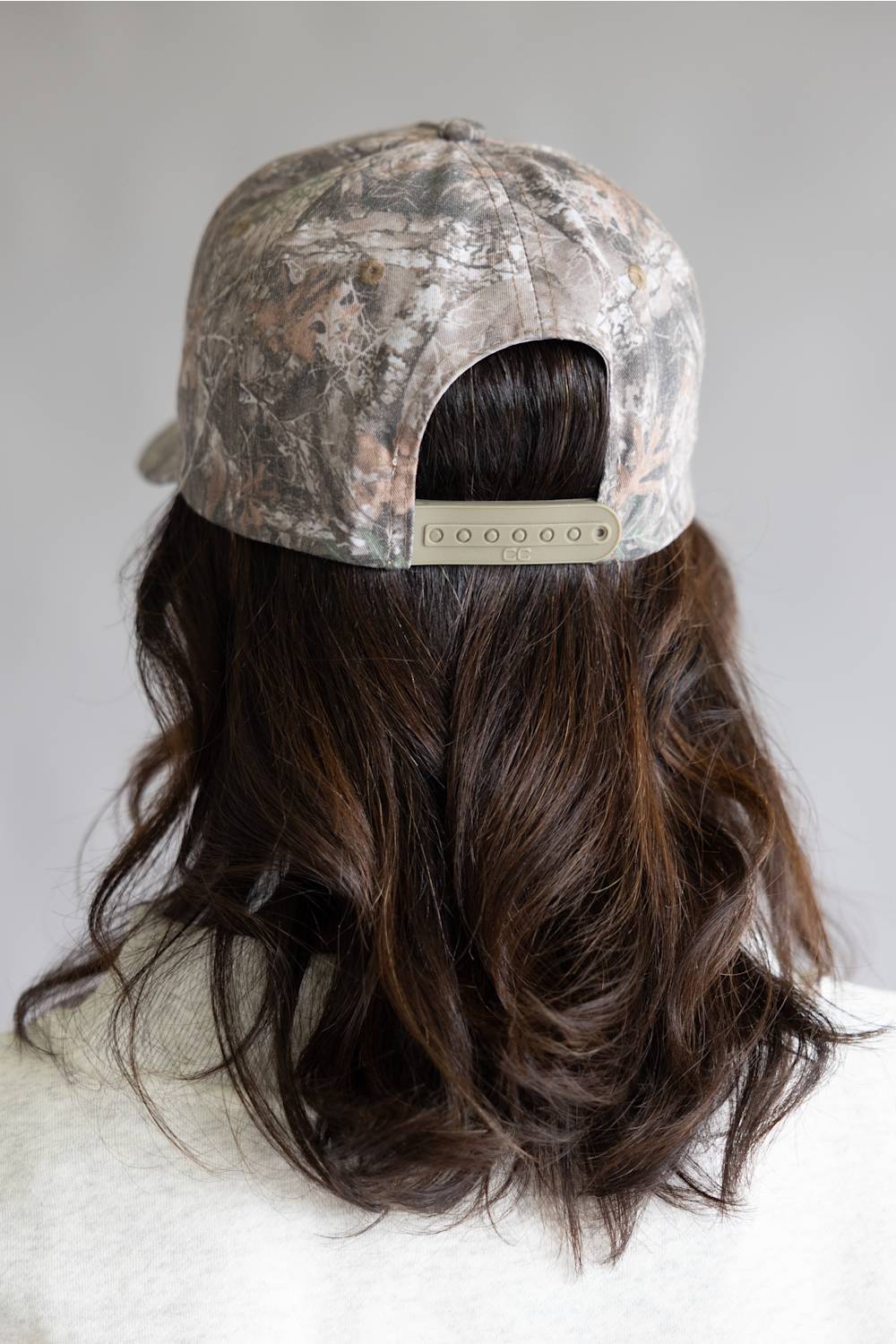 Camouflage cap worn by a woman with long dark hair on a neutral background
