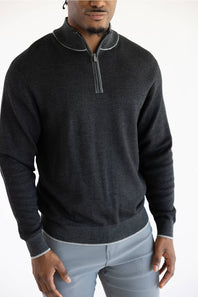 A man wearing a dark charcoal gray quarter-zip sweater with light gray piping details on the collar, cuffs, and hem, paired with light gray trousers.