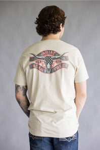 A man viewed from behind wearing a cream-colored t-shirt with a large graphic on the back featuring a steer skull and the text 'ARIAT ROMANCE FREE'.