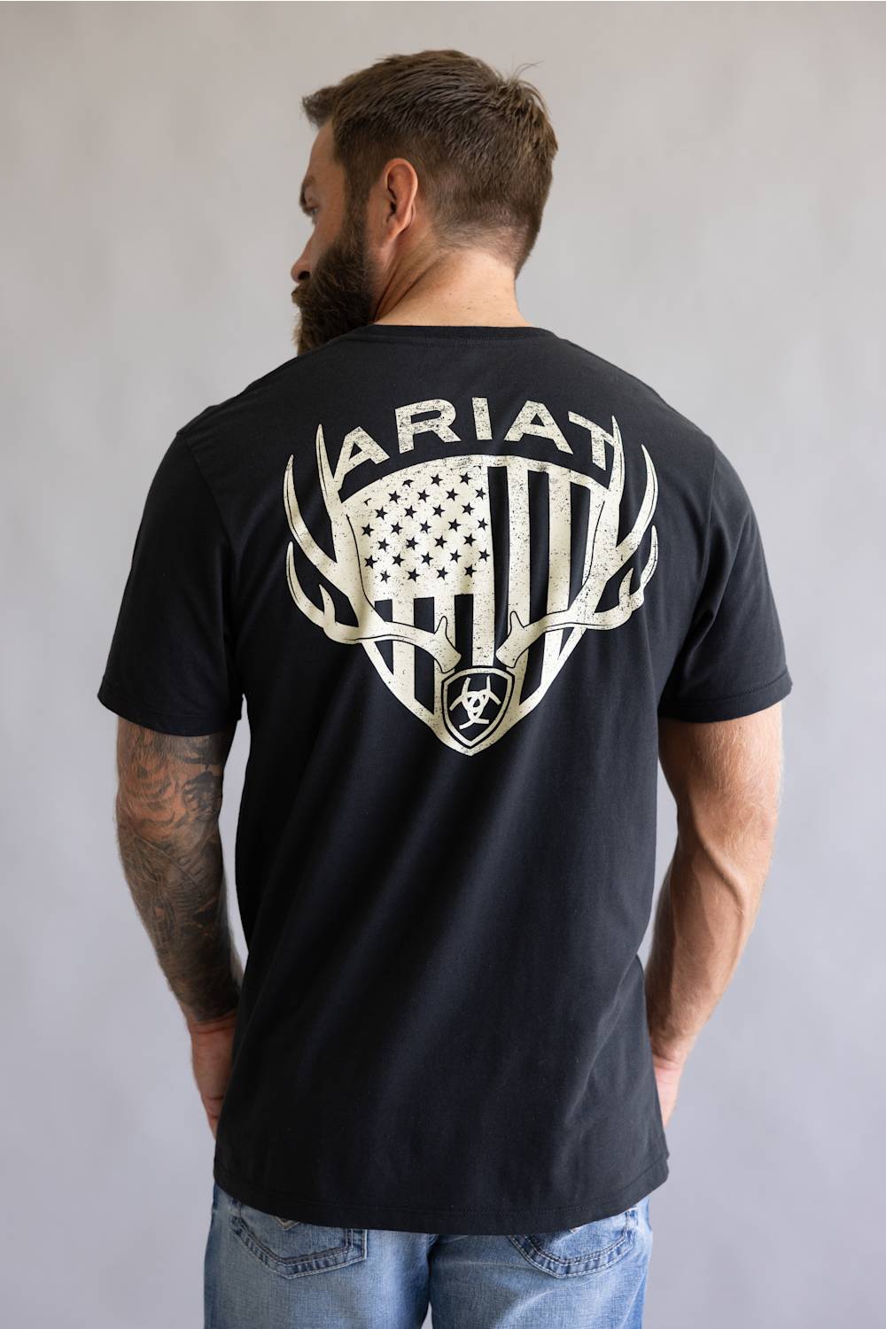 Back of a bearded man wearing a black Ariat t-shirt with an American flag deer antler graphic.