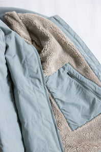 Close-up of a light blue puffer jacket with a beige sherpa fleece lining and a zippered pocket.