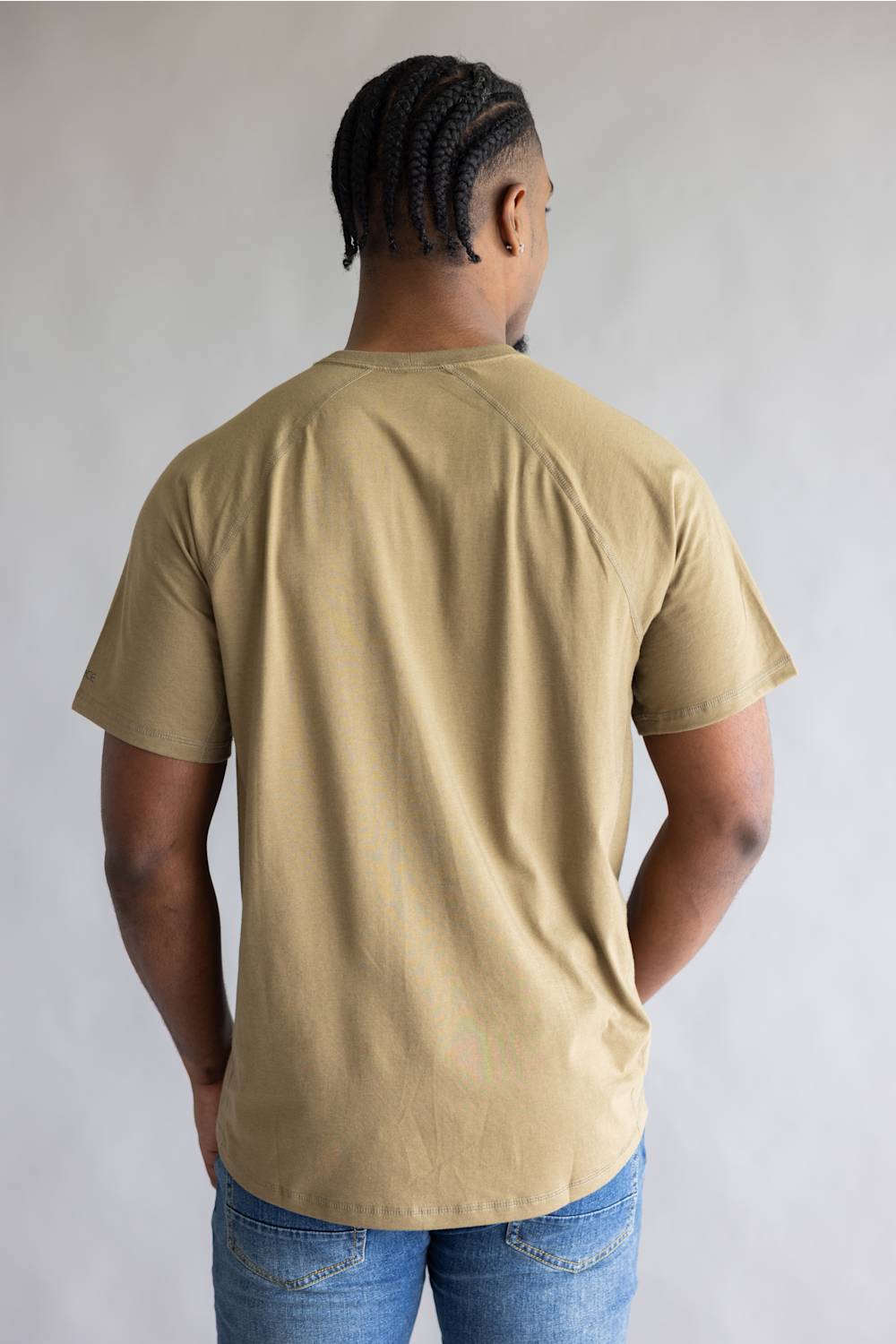 A man viewed from behind wearing a tan short-sleeve t-shirt and blue jeans, standing against a neutral light gray background.