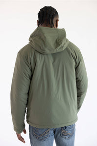 Back view of a man facing away from the camera, wearing a dusty olive green hooded Carhartt zip-up jacket over blue jeans against a plain white background.