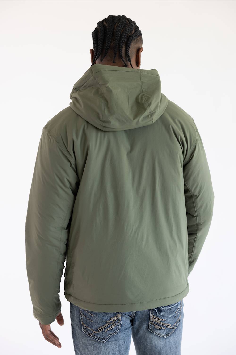 Back view of a man facing away from the camera, wearing a dusty olive green hooded Carhartt zip-up jacket over blue jeans against a plain white background.
