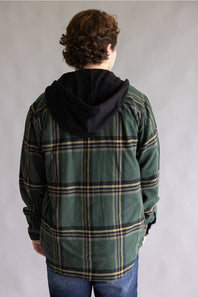 A person viewed from the back wearing a green plaid hooded jacket with a black hood, paired with blue jeans, against a plain gray studio background.