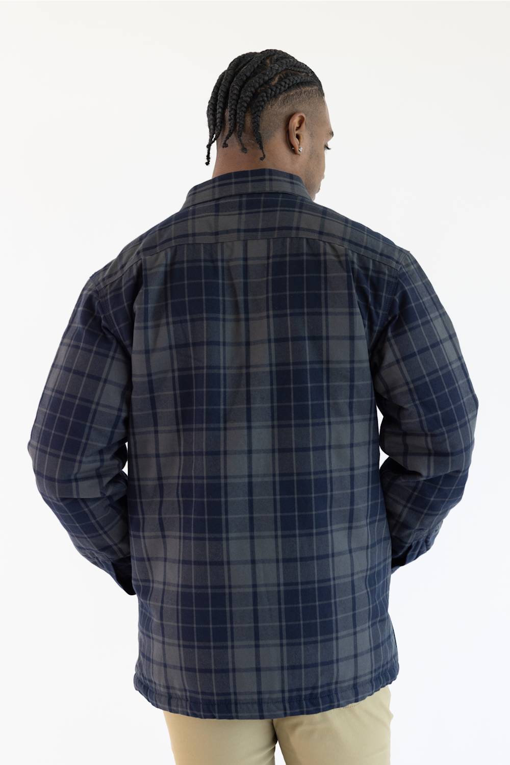 A man viewed from behind wearing a navy blue and gray plaid button-up shirt, paired with beige pants, against a plain white background.