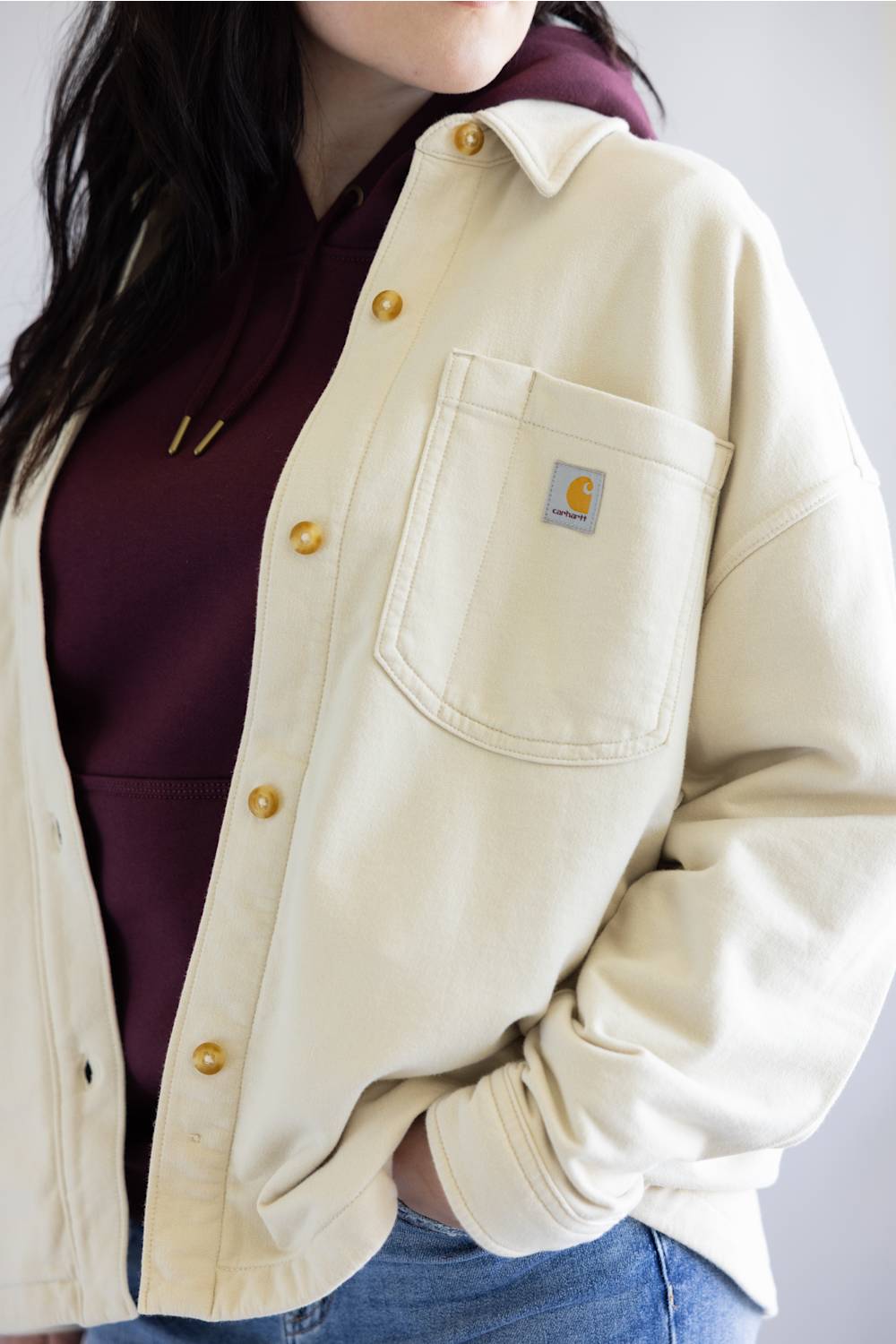 Person wearing a beige Carhartt jacket with a logo on a plain background