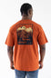 A man viewed from behind wearing a Carhartt orange short-sleeve t-shirt with a large back graphic showing a bear, trees, and the text 'CARHARTT WOOD & WOOD', paired with blue jeans against a white studio background.