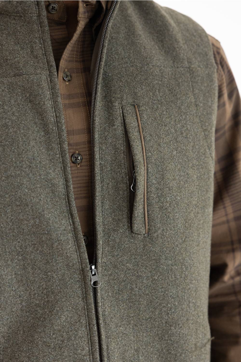 Close-up of an olive green zippered vest worn over a brown plaid button-down shirt, showing a vertical chest pocket.