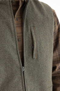 Close-up of an olive green zippered vest worn over a brown plaid button-down shirt, showing a vertical chest pocket.