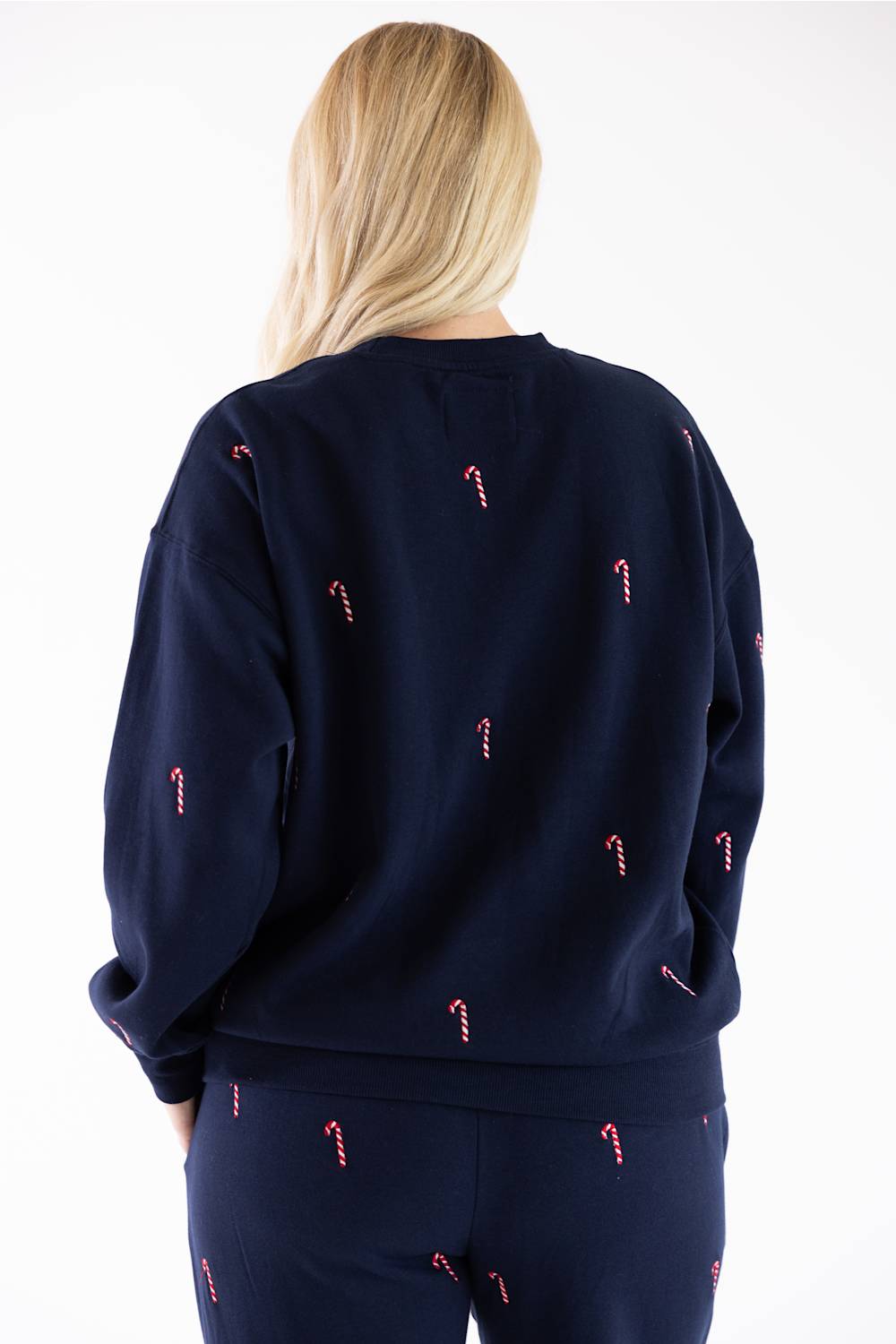 Close-up back view of a navy blue fleece crewneck sweatshirt featuring an all-over embroidered red and white candy cane pattern, with matching sweatpants visible below.