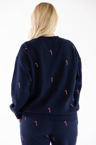 Close-up back view of a navy blue fleece crewneck sweatshirt featuring an all-over embroidered red and white candy cane pattern, with matching sweatpants visible below.