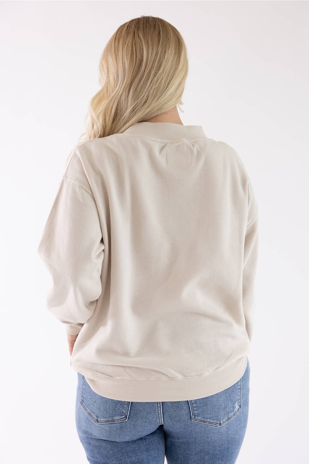 Back view of a woman wearing a beige fleece mock-neck sweatshirt and blue jeans.