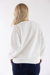 Back view of a blonde woman wearing an ivory 1897 Active Patch Merry and Bright Fleece Sweatshirt and dark blue lounge pants with subtle candy cane patterns.