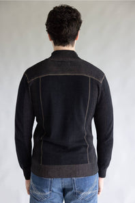 A man viewed from behind wearing a dark charcoal knit sweater with contrasting light brown seam detailing on the shoulders and back, paired with blue jeans, against a neutral gray background.
