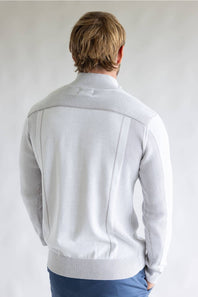 A man viewed from behind wearing a light gray ribbed knit sweater with textured shoulder panels, paired with blue pants, against a plain light gray background.