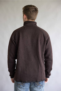 A man viewed from behind wearing a dark brown long-sleeve fleece pullover and blue jeans, standing against a plain light gray studio background.