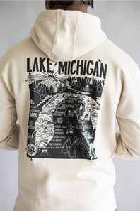 A person shown from the back wearing a cream-colored hoodie with a large black graphic print on the back featuring a map illustration and the text 'LAKE MICHIGAN'.