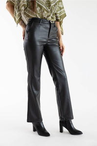 A model is shown from the waist down wearing black faux-leather straight-leg pants, black pointed-toe ankle boots, and a green patterned top against a plain white studio background.