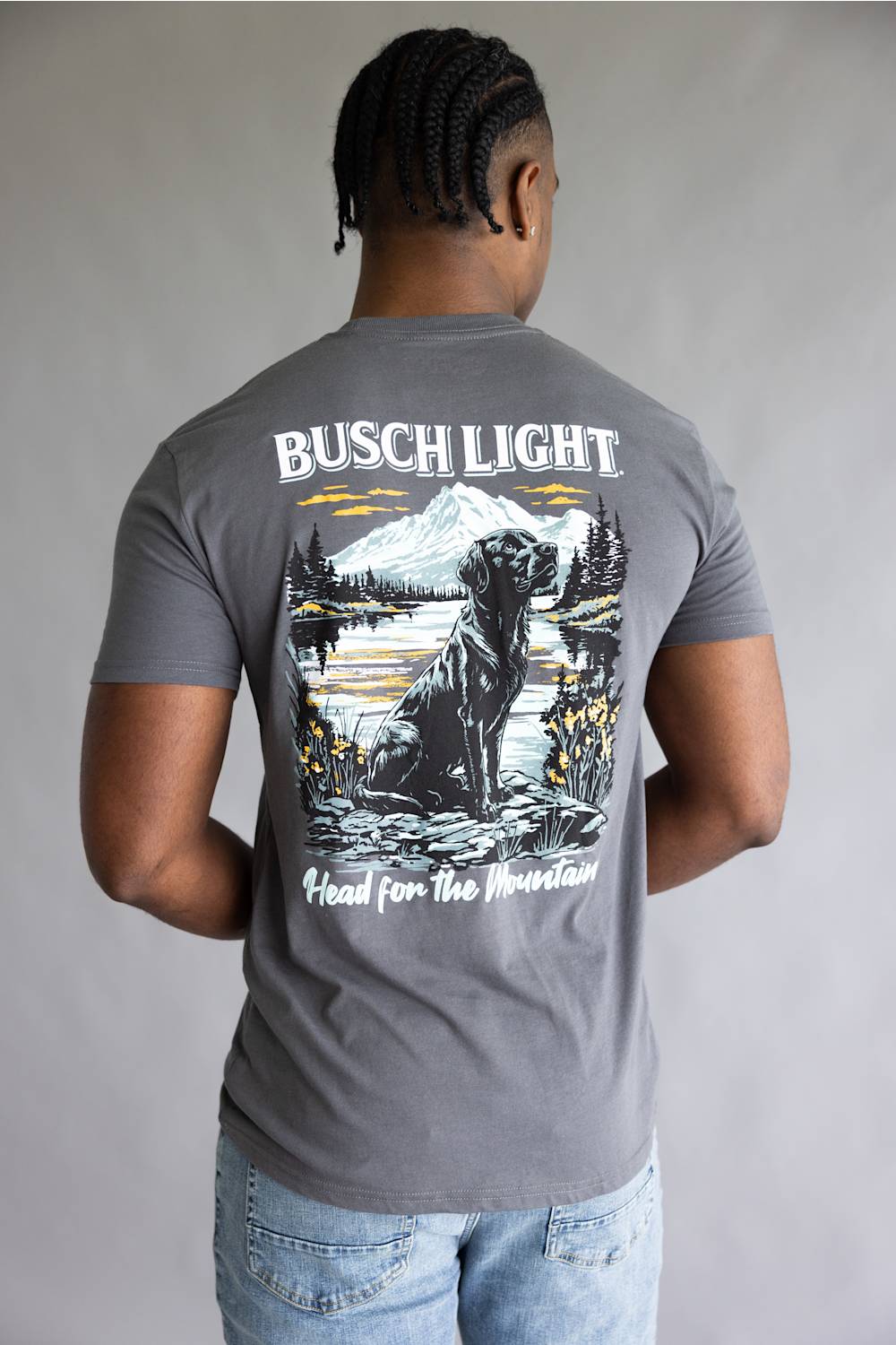 A man viewed from behind wearing a gray t-shirt with a large graphic print on the back featuring a dog, mountain, and lake, with the text 'BUSCH LIGHT' and 'Head for the Mountain'.