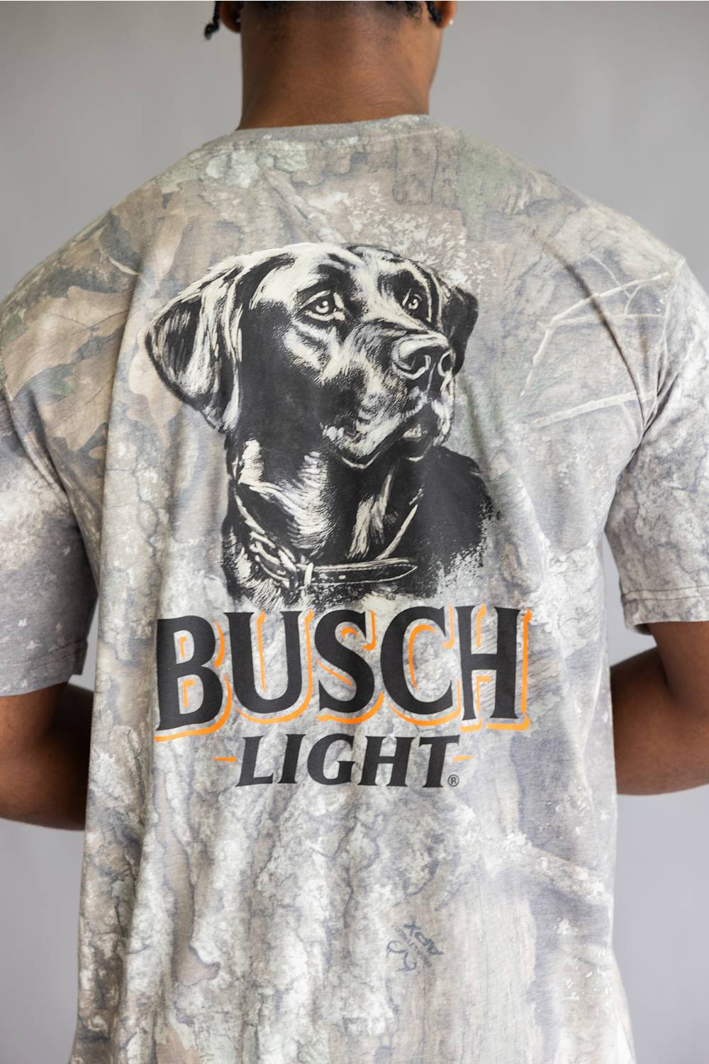 A man viewed from behind wearing a Busch Light t-shirt with a large black and white dog graphic and the brand name printed on the back.