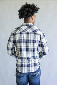 A man viewed from behind wearing a long-sleeve plaid button-up shirt in white, navy, and gray, paired with blue jeans, against a plain light gray background.