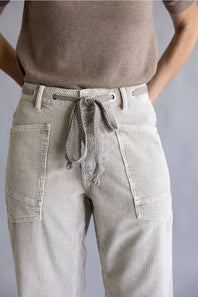 Close-up of a person wearing light beige corduroy pants with a drawstring waist, side cargo pockets, and a taupe knit top against a plain gray background.