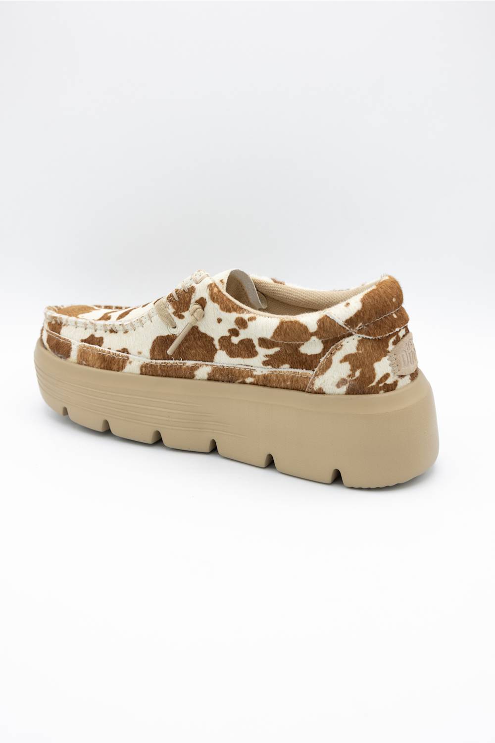 A single slip-on platform shoe featuring a brown and cream cow-print pattern on the upper and a chunky beige sole, shown from a side-rear angle against a plain white background.