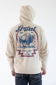 A person shown from the back wearing a light beige hoodie with a large blue and red graphic print featuring a bison and the text 'Ariat Boot Co.' and 'Strength Unity and Heritage,' paired with dark blue jeans against a plain white background.