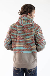 A man viewed from the back wearing a hooded sweatshirt with a multicolor geometric pattern on the upper body and sleeves, and a solid taupe lower body, paired with blue jeans against a white studio background.