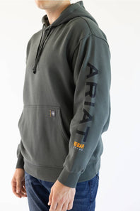 A man wearing a dark gray hoodie with 'ARIAT' printed vertically in black on the right sleeve and a small orange logo near the pocket, paired with blue jeans against a plain white background.