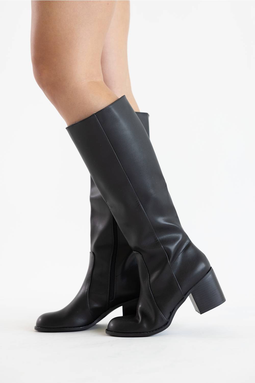 Black leather knee-high boots with a block heel, shown on a model's legs against a plain white studio background.