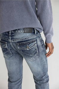 Close-up back view of a person wearing light-wash blue denim jeans and a ribbed blue-gray sweater against a plain light background.