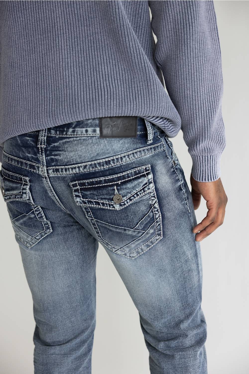 Close-up back view of a person wearing light-wash blue denim jeans and a ribbed blue-gray sweater against a plain light background.