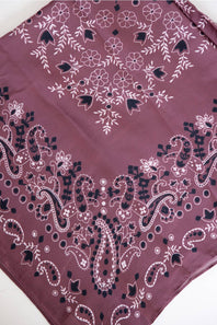 A square bandana featuring a dusty plum purple base with white and black paisley and floral patterns, laid flat on a white surface.