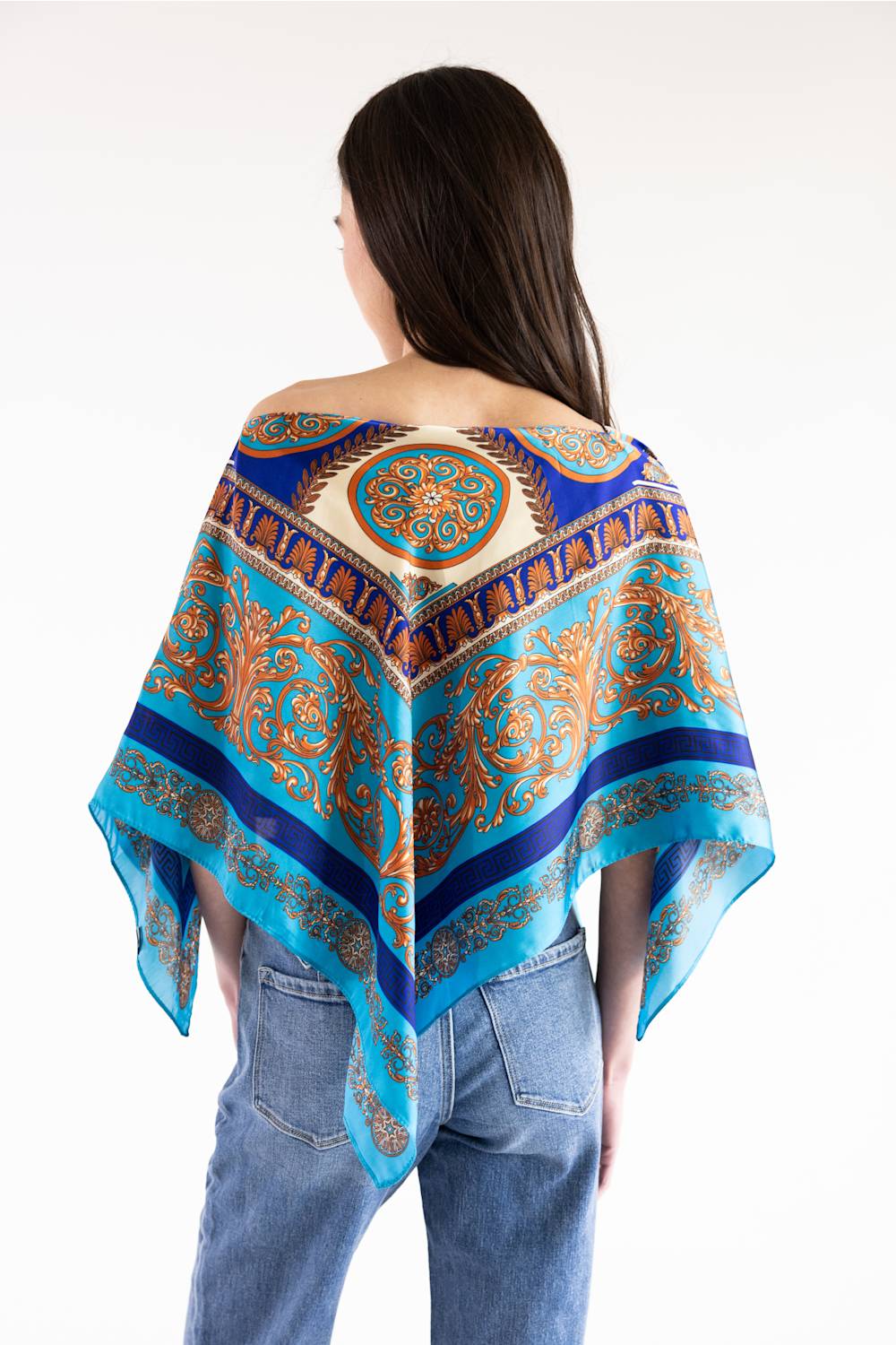 A woman shown from the back wearing a vibrant blue and orange paisley-patterned shawl draped over her shoulders, paired with light-wash blue jeans against a plain white background.