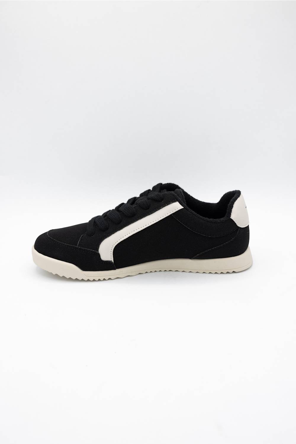 A black low-top sneaker with a contrasting white side stripe, black laces, and a white sole, shown from a side profile view against a plain white background.