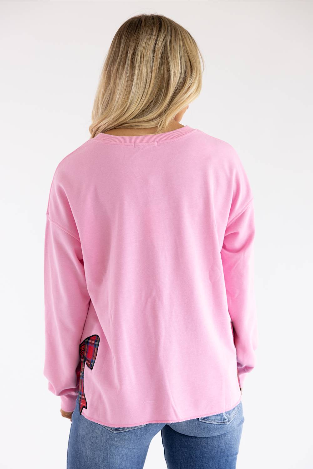 A woman viewed from behind wearing a light pink long-sleeve crewneck sweatshirt and blue jeans against a plain white background.