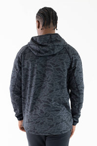 A man viewed from behind wearing a dark gray and black camouflage-patterned hooded sweatshirt against a plain white background.