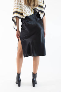 A model shown from the back wearing a black satin midi skirt with a side slit, paired with a patterned top and black ankle boots, against a plain white background.
